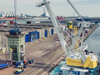 View of a busy industrial port with warehouses, cranes, trucks, and ships along the waterfront.