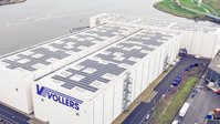 Luftaufnahme eines großen Lagergebäudes mit Solarmodulen auf dem Dach in der Nähe des Wassers.