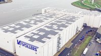 Luchtfoto van een groot magazijngebouw met zonnepanelen op het dak nabij het water.