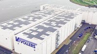 Aerial view of a large warehouse building with solar panels on the roof near the waterfront.