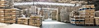 Large warehouse filled with stacked jute coffee bags on pallets, forming aisles under a high industrial ceiling.