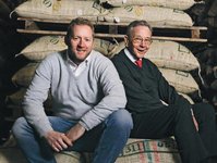 Christian Vollers and his father Lüder Vollers sit smiling on a stack of coffee bags and look at the camera.