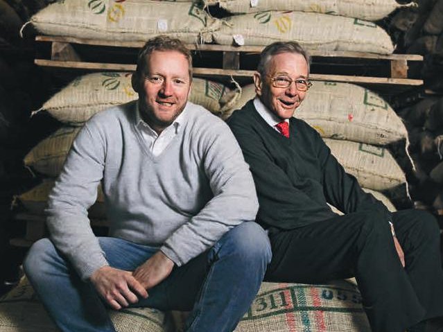 Christian Vollers and his father Lüder Vollers sit smiling on a stack of coffee bags and look at the camera.