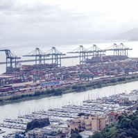 Luftaufnahme eines Containerterminals mit gestapelten Containern und Kränen entlang des Wassers.
