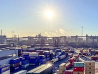 View of the Köhlbrand Bridge spanning the port of Hamburg, with container terminals and cranes in the foreground at sunset.
