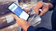Person scanning a barcode on stacked cargo using a smartphone in a warehouse.