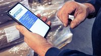 Persoon scant een barcode op gestapelde goederen met een smartphone in een magazijn.