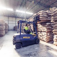 A woman driving a forklift in a warehouse. She's picking a coffee bag with the fork