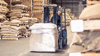 Warehouse interior with stacked pallets of bagged goods and wide storage aisles.