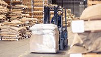 Binnenaanzicht van een magazijn met gestapelde pallets met zakken en brede gangpaden.