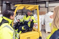 Three people talking in a warehouse, one sitting in a forklift.