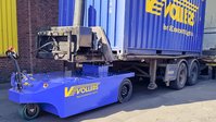 Blue container transport vehicle carrying a shipping container in a logistics yard.