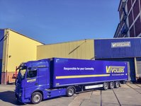 Blue Vollers truck parked in front of a warehouse building.