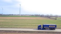 Vollers truck driving along a road in a rural landscape with wind turbines in the background.