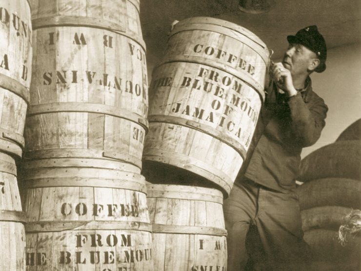 Historic sepia photo of port workers standing next to large coffee barrels.
